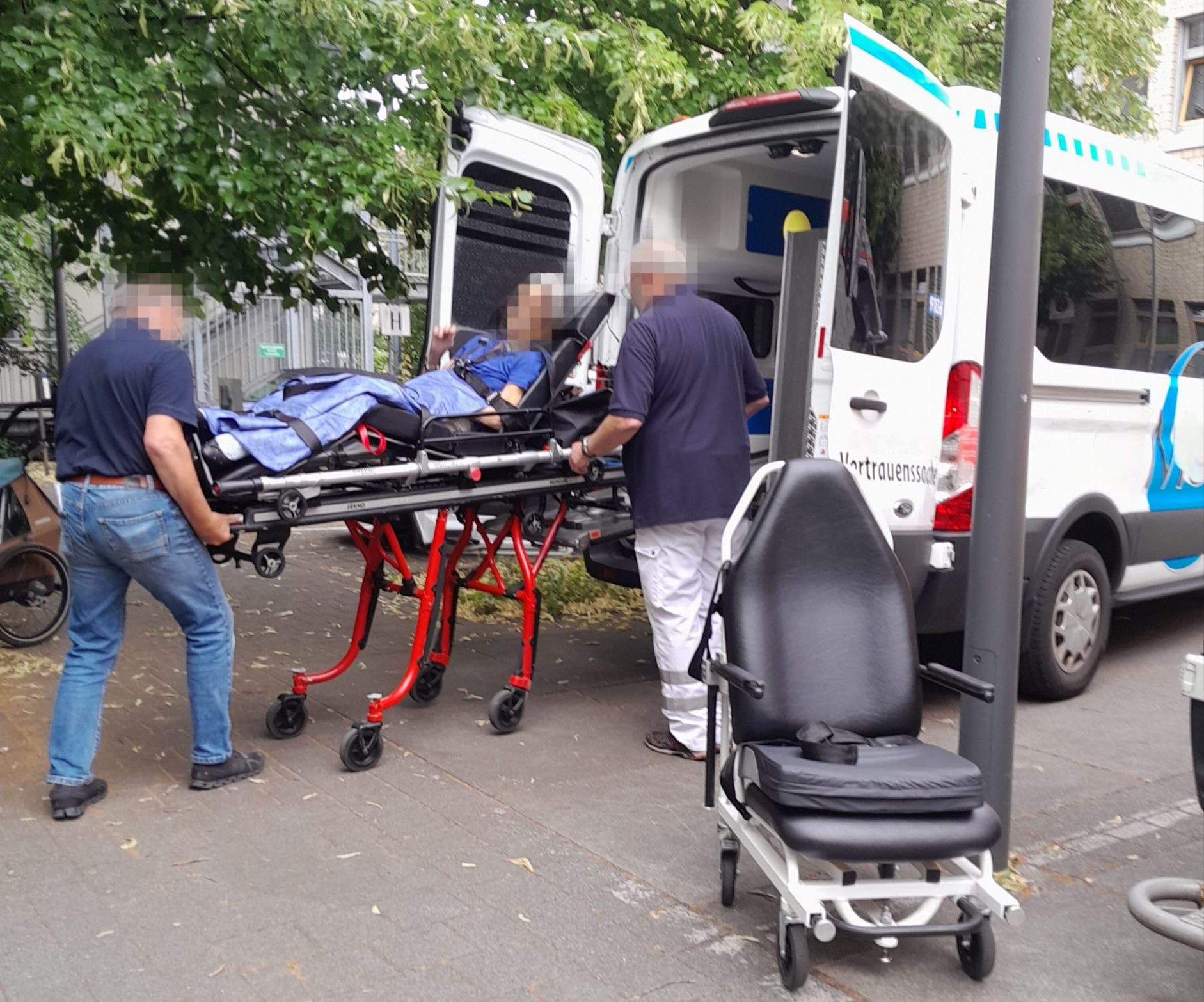 Zwei Männer in Freizeitkleidung und Turnschuhen schieben einen schwerkranken Patienten in einen Mietliegewagen. Foto: privat